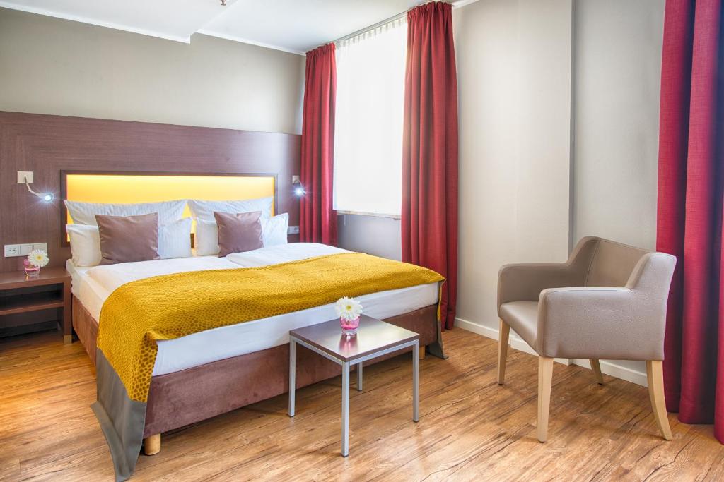 a bedroom with a bed, chair, desk and a lamp at Leonardo Hotel München City Center in Munich