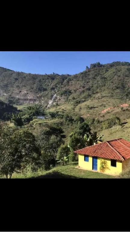 a yellow house with a red roof in front of a mountain at Refúgio, Aconchego, Aonde nasce o sol e Cachoeira! in Mercês