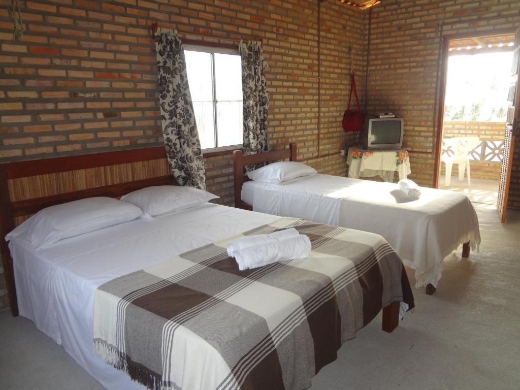 two beds in a room with a brick wall at Pousada Sol e Mar in Parajuru