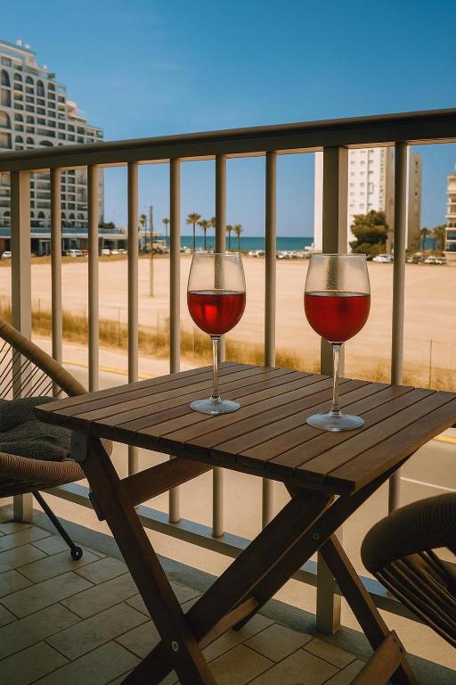 two glasses of red wine sitting on a wooden table on the beach at Cataleya Apartment in Cullera