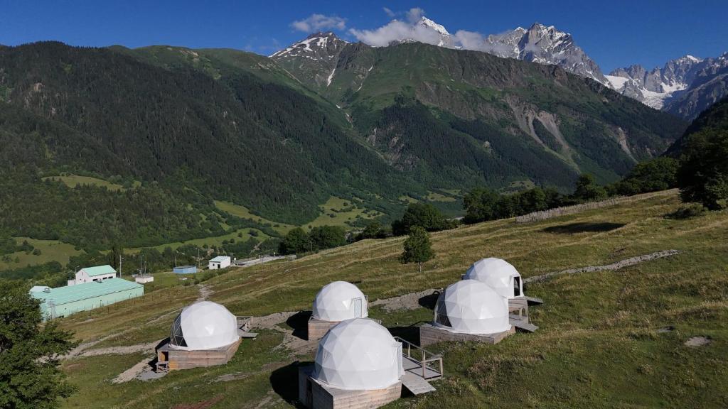 a group of observatories on a hill with mountains in the background at Glamp Peaks Mestia in Mestia