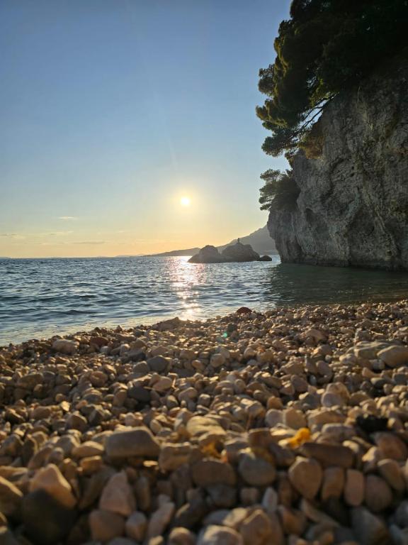 a rocky beach with the sun setting over the water at Rajčić Apartmani in Omiš