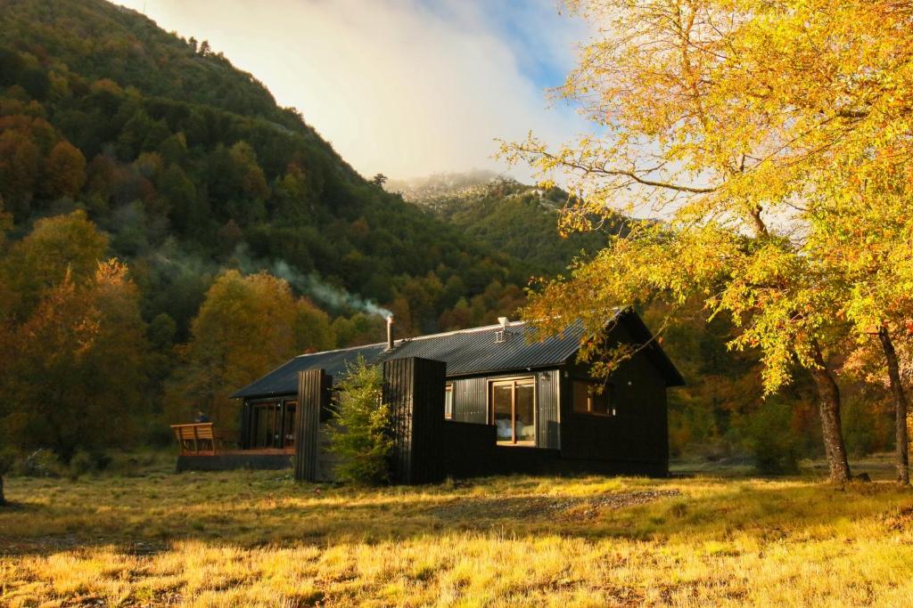 a black cabin in a field with a mountain at Casa Las Raíces - Relajo con tinaja y vista al volcán, a minutos de Corralco in Malalcahuello