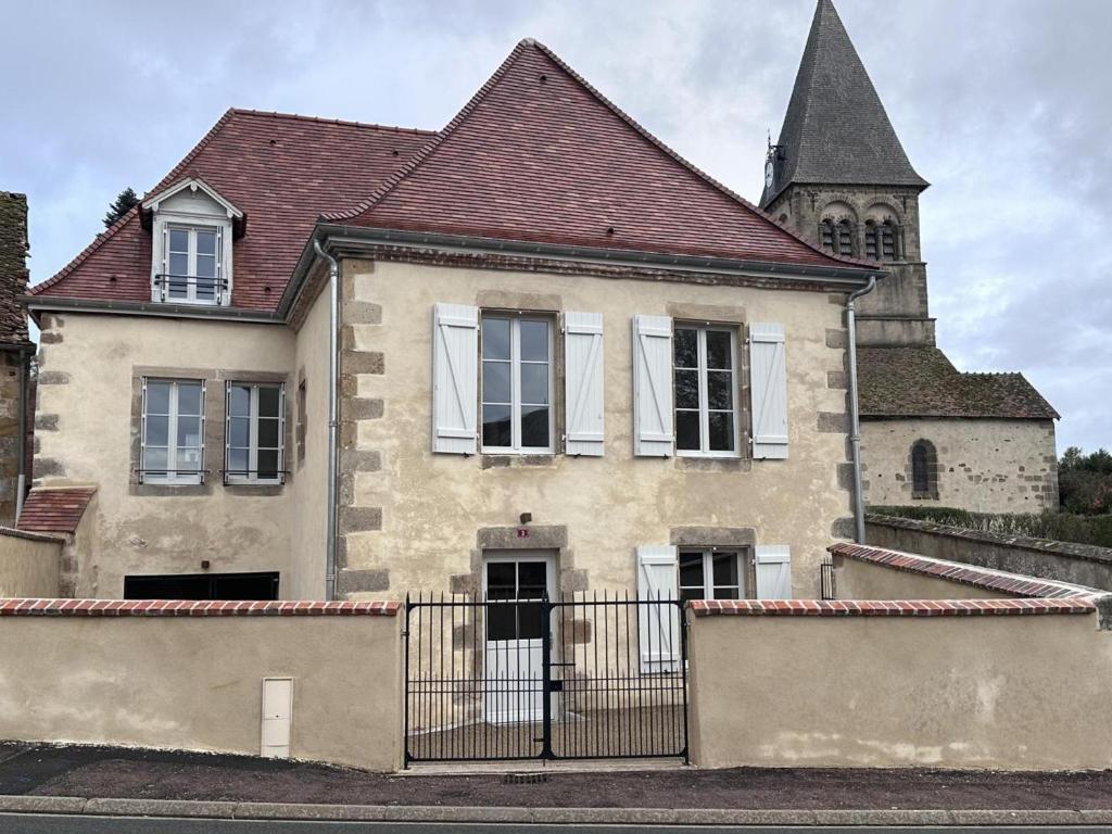 an old house with a fence in front of a church at Gîte historique rénové avec jardin et WiFi - FR-1-489-571 in Theneuille