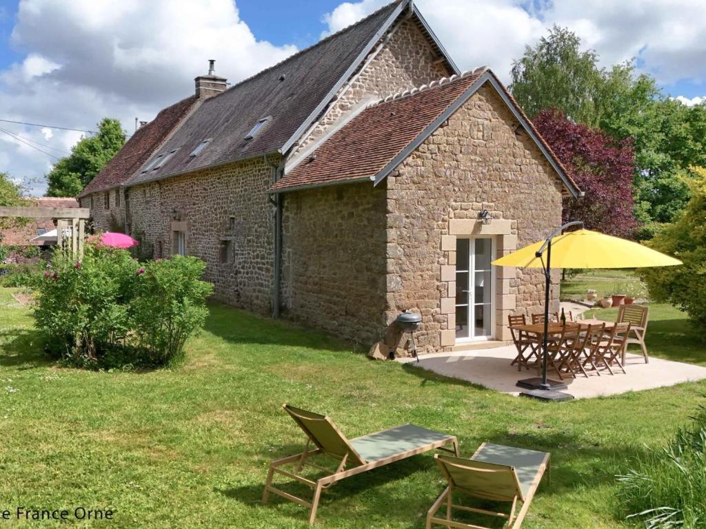 a stone cottage with a table and chairs and an umbrella at Longère avec Jardin Exotique, Terrasse et Wifi Inclus - FR-1-497-246 in Saint-Fraimbault