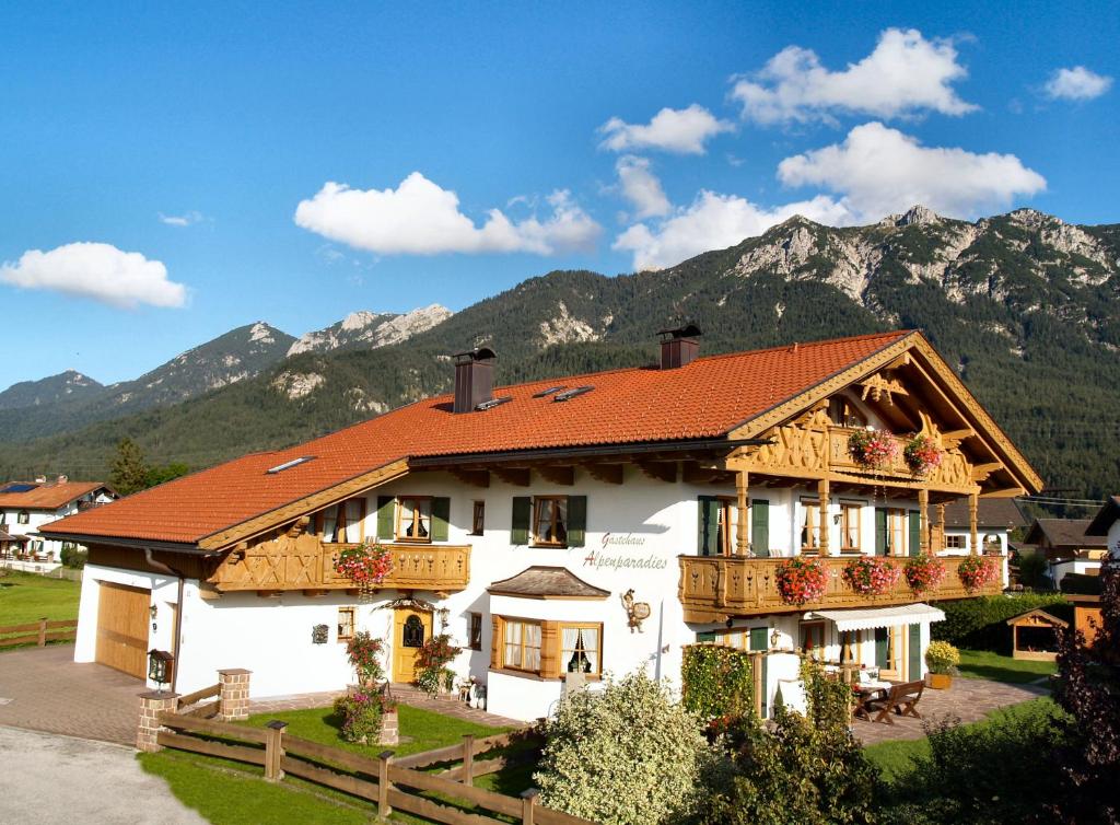 a white house with a red roof with mountains in the background at Gästehaus Alpenparadies in Krün