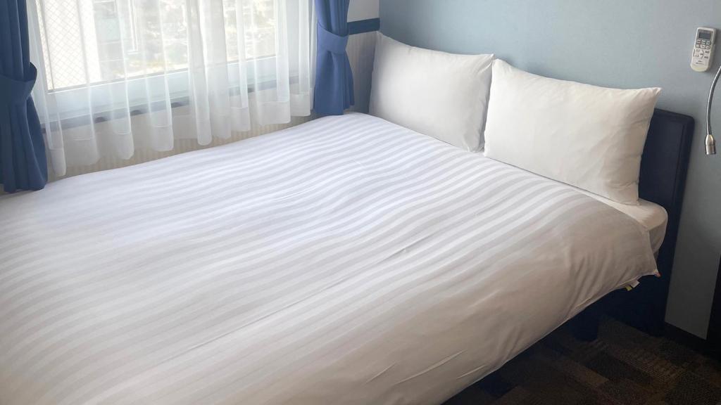Toyoko Inn Saitama Iwatsuki Ekimae في سايتاما: سرير كبير بملاءات بيضاء ونافذة