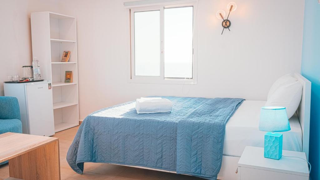 a bedroom with a bed with a blue blanket and a window at Arka - Studio B in Anfah