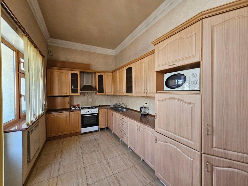 a large kitchen with wooden cabinets and a microwave at Rijkov St Apartment in Gyumri
