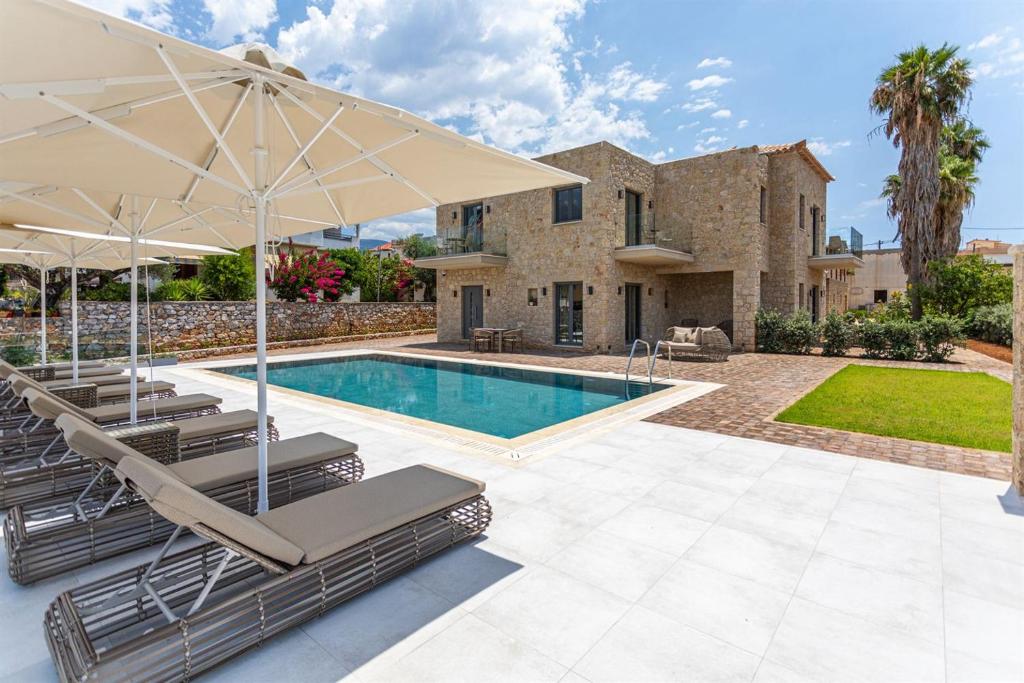 a villa with a swimming pool with chairs and an umbrella at Ampeli Villas in Stoupa
