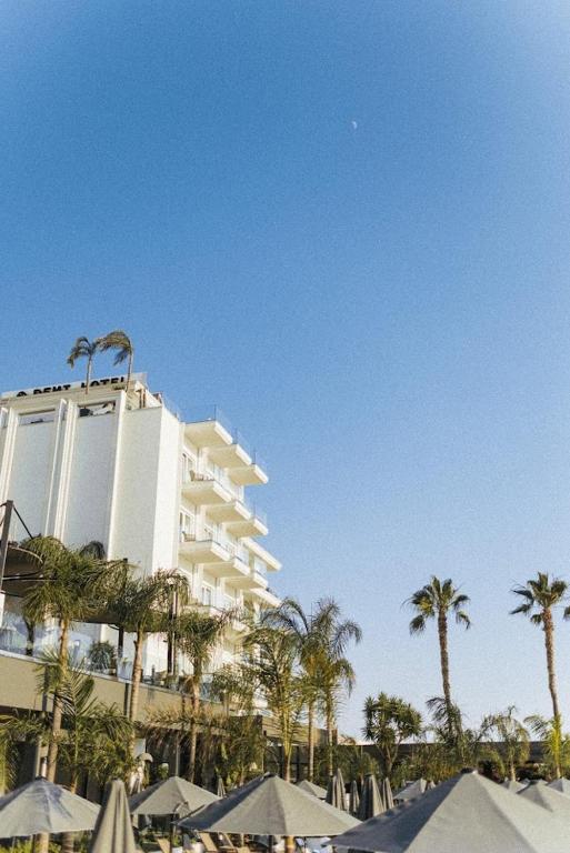 a large white building with palm trees and umbrellas at Demi Hotel in Sarandë
