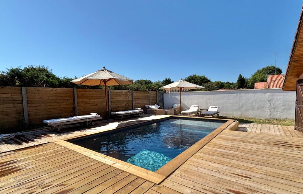 une piscine avec une terrasse en bois et un parasol dans l'établissement Villa Terrama Capbreton, à Capbreton