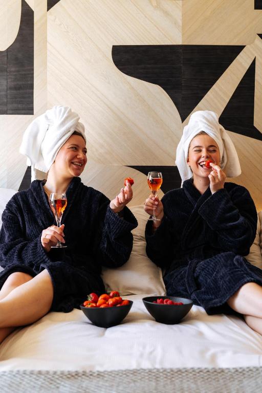 ニーウポールトにあるCosmopolite Hotel Nieuwpoort-Badのワインとフルーツのグラスを持ってベッドに座っている2人の女性