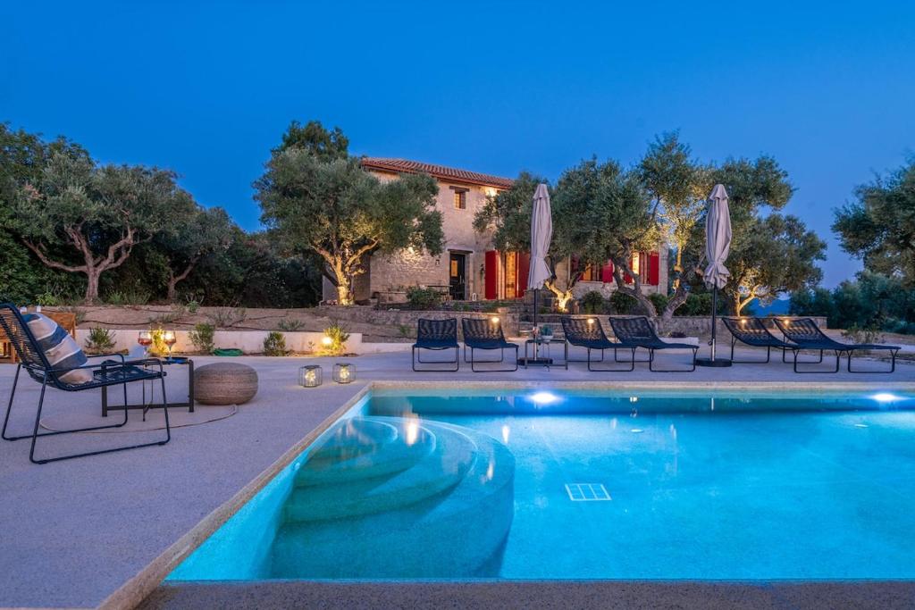 a swimming pool with chairs and umbrellas in front of a house at Geracasa Stone Villa in Méson Yerakaríon