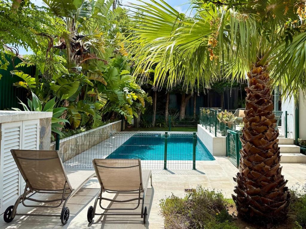deux chaises et un palmier à côté d'une piscine dans l'établissement Charming cottage, pool & garden by Guincho beach, à Aldeia de Juso