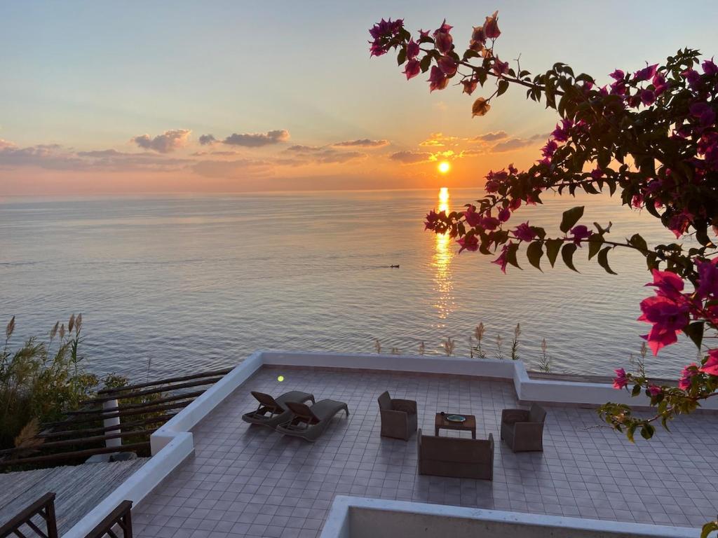 a sunset over the water with chairs and a table at Eolian Villa Mare - Floating over the sea in San Salvatore