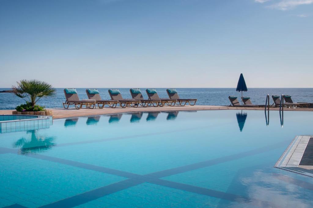 a swimming pool with chairs and the ocean in the background at Pyrgos Beach Hotel Apartments in Malia