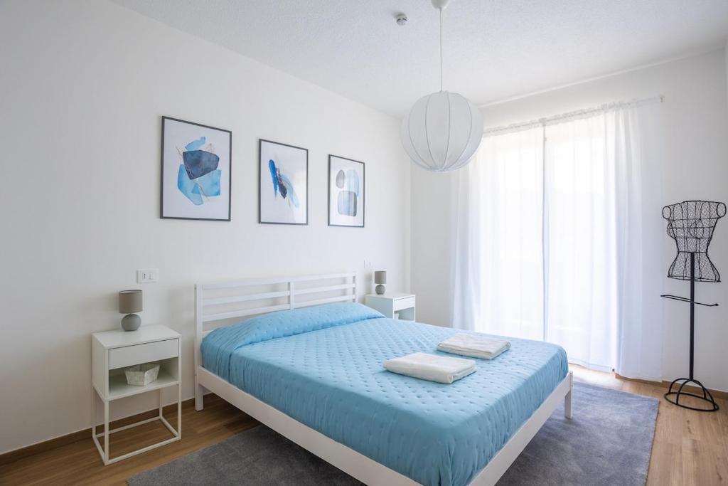 a white bedroom with a blue bed and a window at The Window on the Lake - Balcony Beaches Playground in Brusimpiano