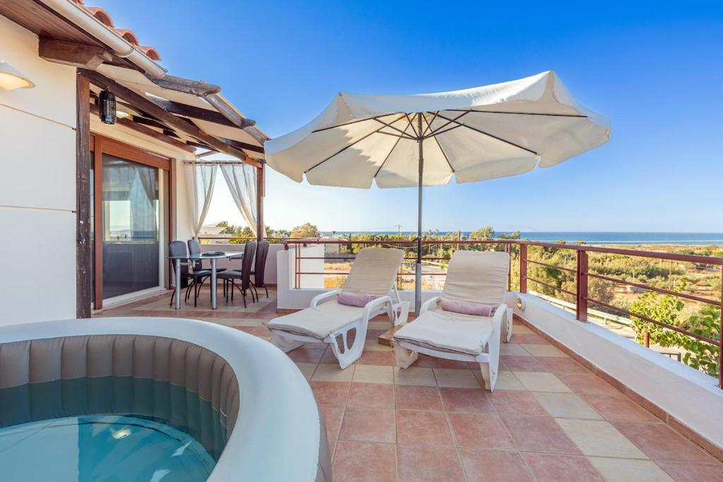 un patio con bañera de hidromasaje, sillas y sombrilla en Chris Sea View Apt with Hot Tub, en Gouves