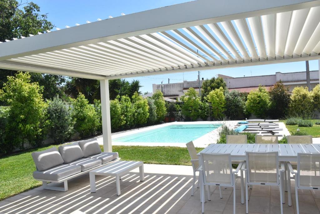 une pergola blanche avec une table et des chaises ainsi qu'une piscine dans l'établissement Casa del Sol Luxury Estate Puglia, à Leporano Marina