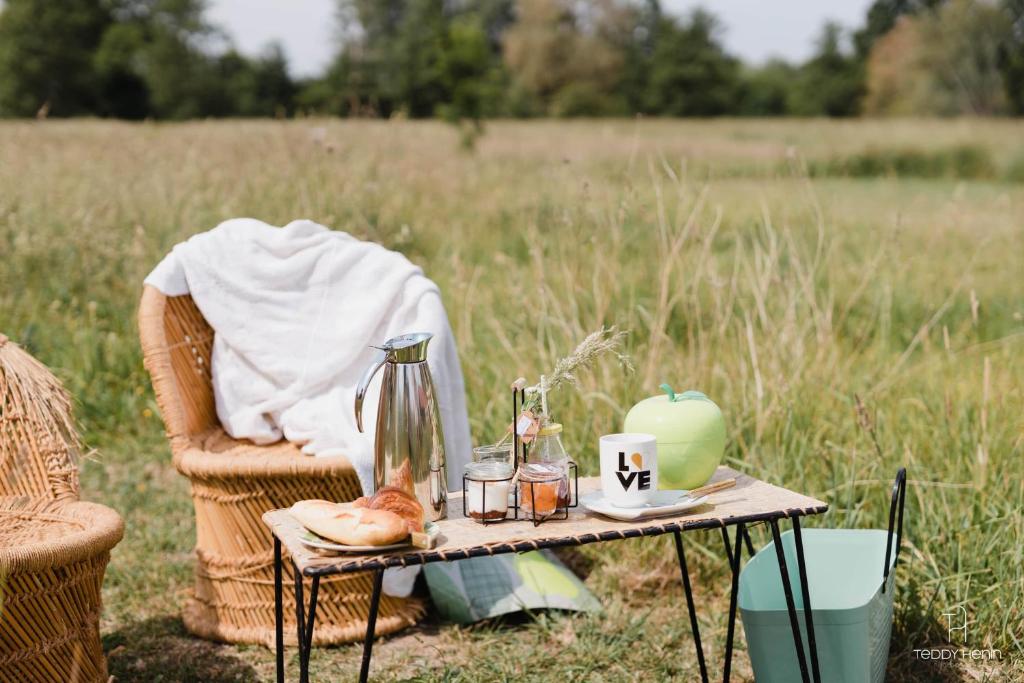 une table dans un champ avec une couverture et une table avec une table dans l'établissement Les Aires en Scènes au bord de l'eau, à Épagne-Épagnette