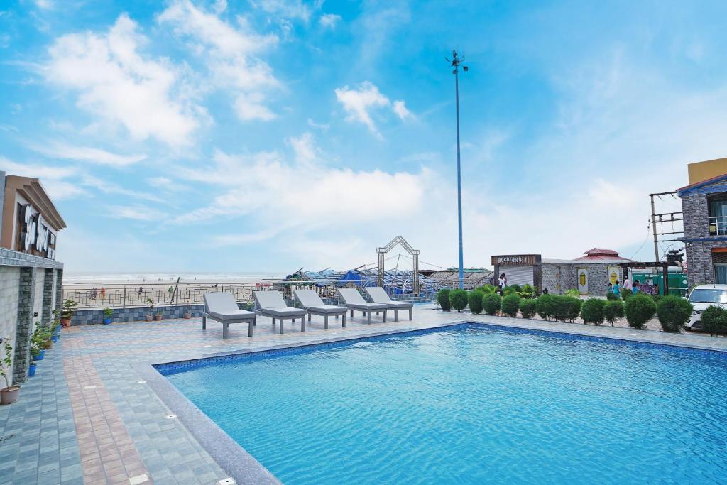 a swimming pool with chairs and the beach in the background at Goa Beach Resort ON Beach in Mandarmoni