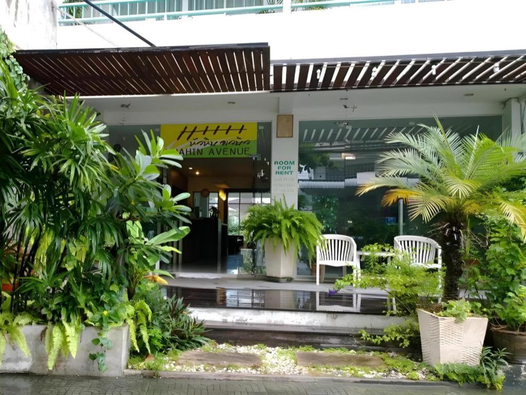 a building with two white chairs and palm trees at Hua Hin Avenue Hotel in Hua Hin
