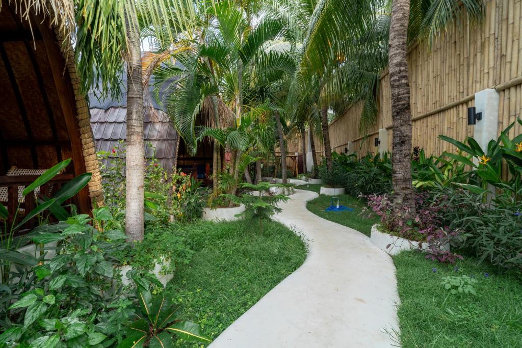 a walkway in a garden with palm trees and plants at Tricky Trees Sunset Bungalows in Gili Air