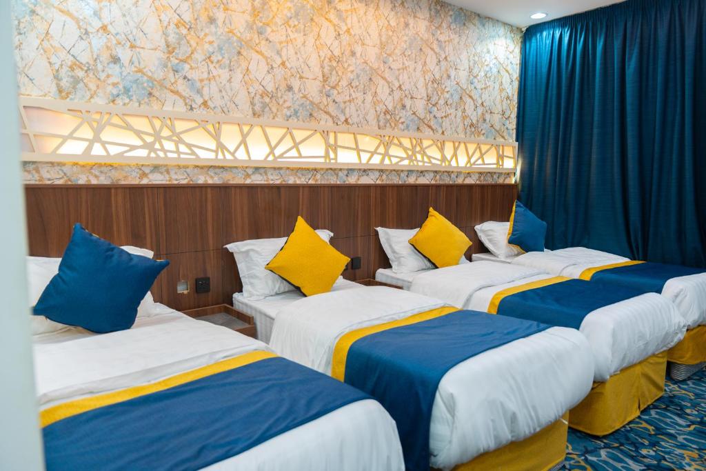 three beds in a room with blue and yellow pillows at فندق برادايس لاند الزهراء Paradis Land Hotel ALzhra in Az Zahrāʼ