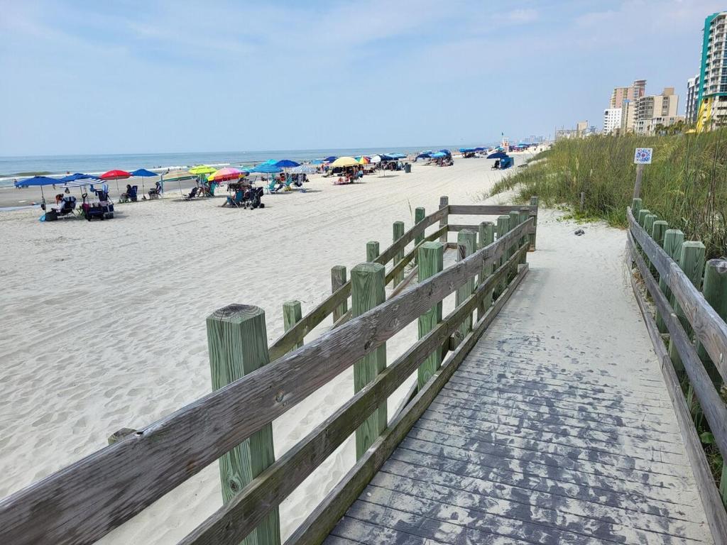 a wooden fence on a beach with people on it at Crescent Vintage Cottage in Myrtle Beach