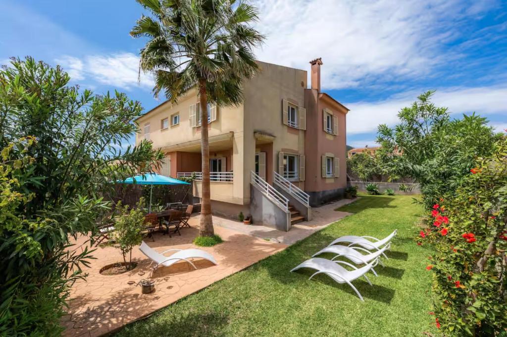 an exterior view of a house with lawn chairs and palm trees at Casa Luz Cala Rajada in Cala Ratjada