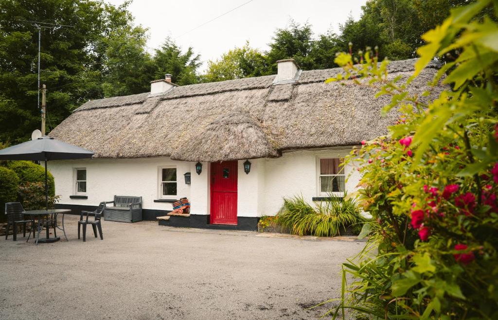ein weißes Haus mit einem Strohdach und einer roten Tür in der Unterkunft Longford Holiday Kitty Kiernan's Self Catering Thatch Cottage in Longford