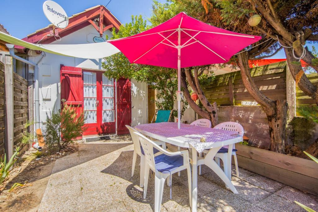 une table et des chaises avec un parasol rose dans l'établissement Charmante maison ancienne, à Lacanau-Océan