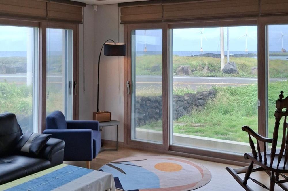 a living room with a couch and chairs and windows at Jeju Noeul Bori Pension in Jeju