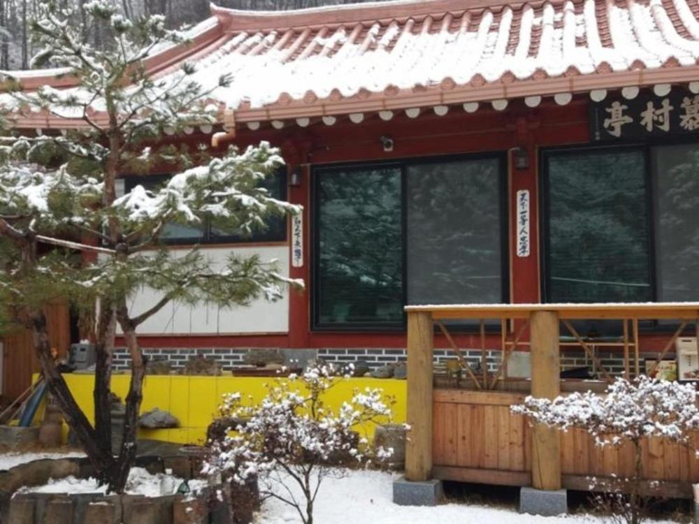 a house covered in snow in front of a building at Chiak Moutain Hanok Pension in Wonju