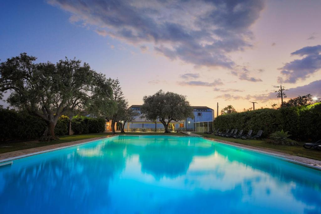 una gran piscina azul con árboles y un edificio en Tenuta Arangio Agriturismo Vendicari, en Casa Maccari