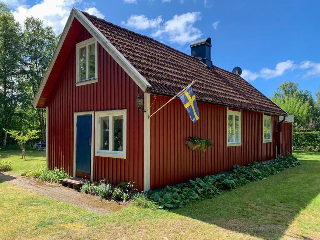 ein rotes Haus mit einer Flagge davor in der Unterkunft Family-Friendly Cottage Near The Sea In Ugglarp in Heberg