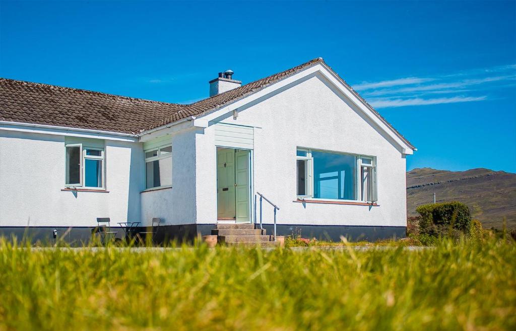 a white house with a green door in a field at Creag Dubh in Camastianavaig