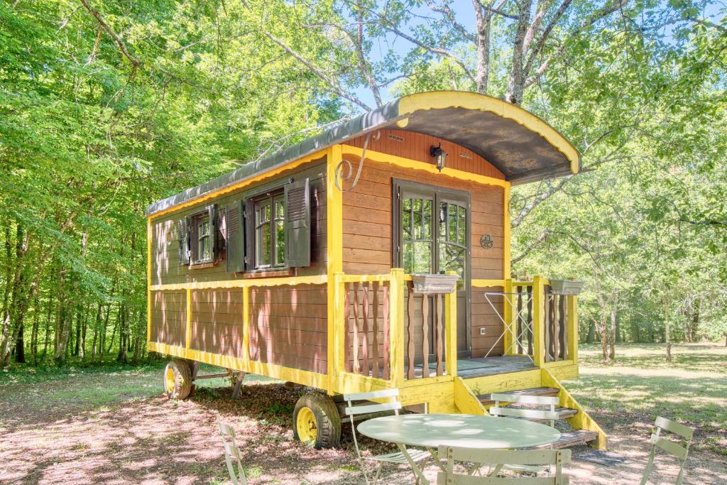 une petite maison jaune avec une table dans une forêt dans l'établissement La Roulotte Jaune, à Monsac