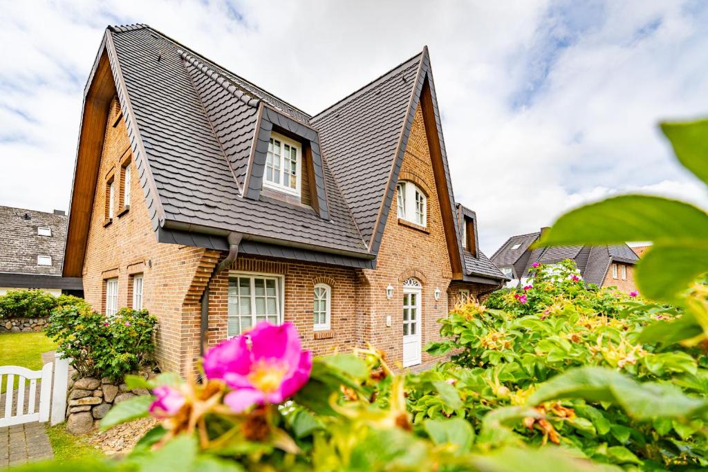 a brick house with a black roof and a pink flower at Strandpirat in Wenningstedt