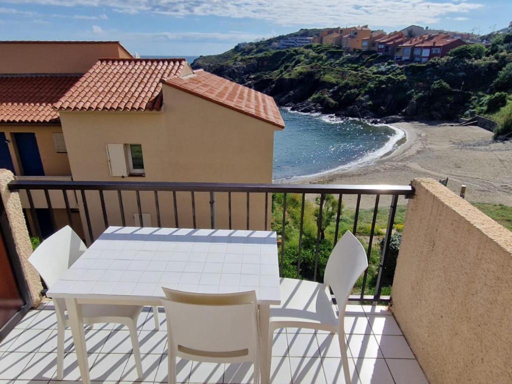 - une table et des chaises blanches sur un balcon avec une plage dans l'établissement Collioure T2 bord de mer avec parking - FR-1-309-514, à Collioure