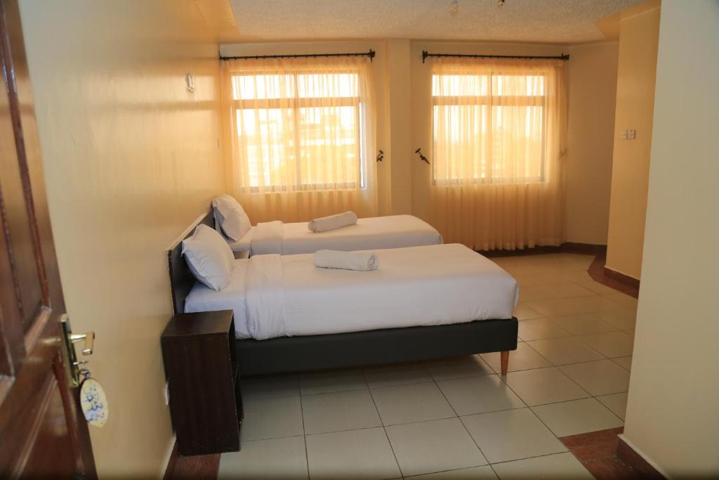 a bedroom with two beds and two windows at Alma Hotel, Kitengela in Nairobi