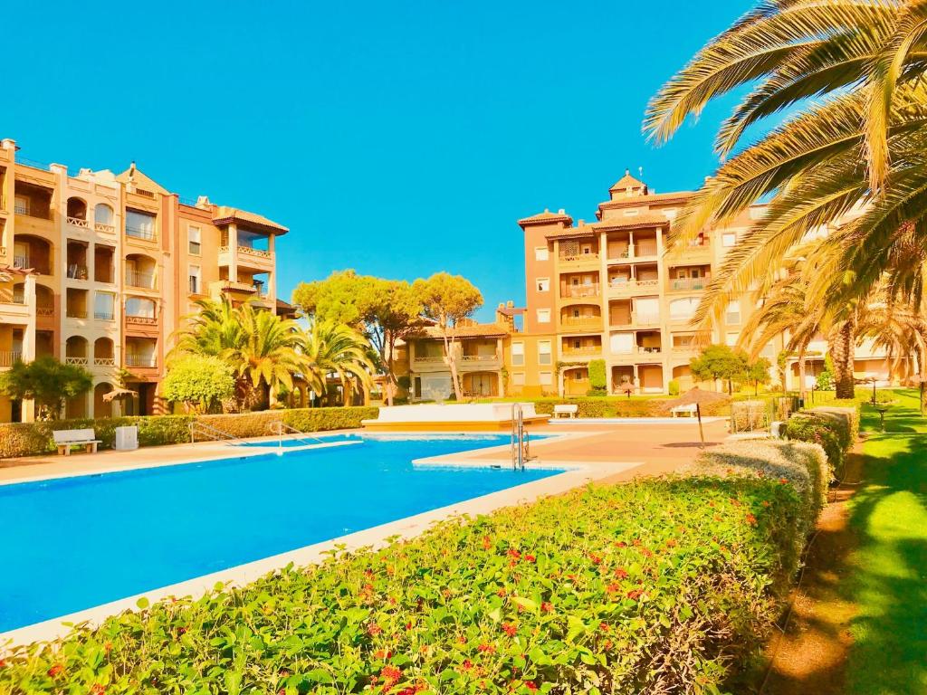 a swimming pool in a resort with palm trees and buildings at Alcaraván, Isla Canela - By AC REAL in Isla Canela