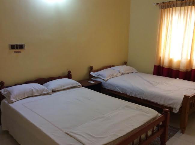 two twin beds in a room with a window at Redrose Service Apartment in Kannur
