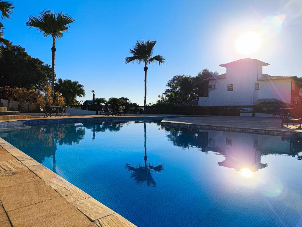 a swimming pool with palm trees and a building at Suites Buzios in Búzios