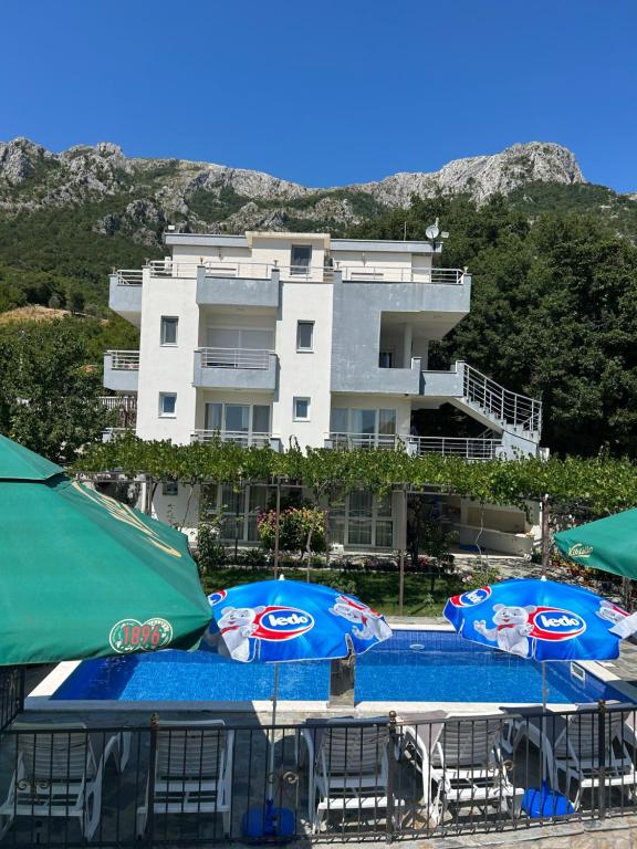 two blue umbrellas on a beach in front of a building at Apartmani Planinska Idila in Bar
