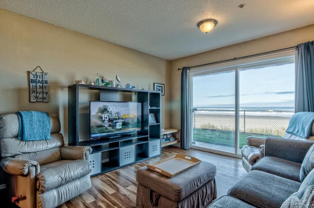 Una sala de estar con televisión, sofá y sillas. en Modern Ground Floor Beachfront Condo Suite - Sleeps 4 - Pool and Sauna, en Lincoln City