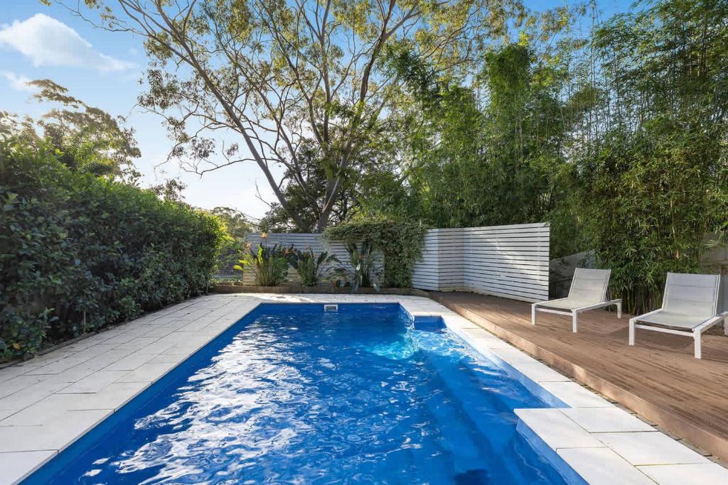a swimming pool in a backyard with two white chairs at Cottage on Riv - Winter Holiday Mid-Week Special in Terrigal