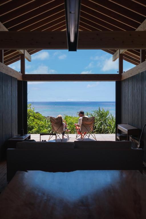 two people sitting in chairs in a room with a view of the ocean at ViLLA SHiNAHA ヴィラシナハ 与論島 in Yoron