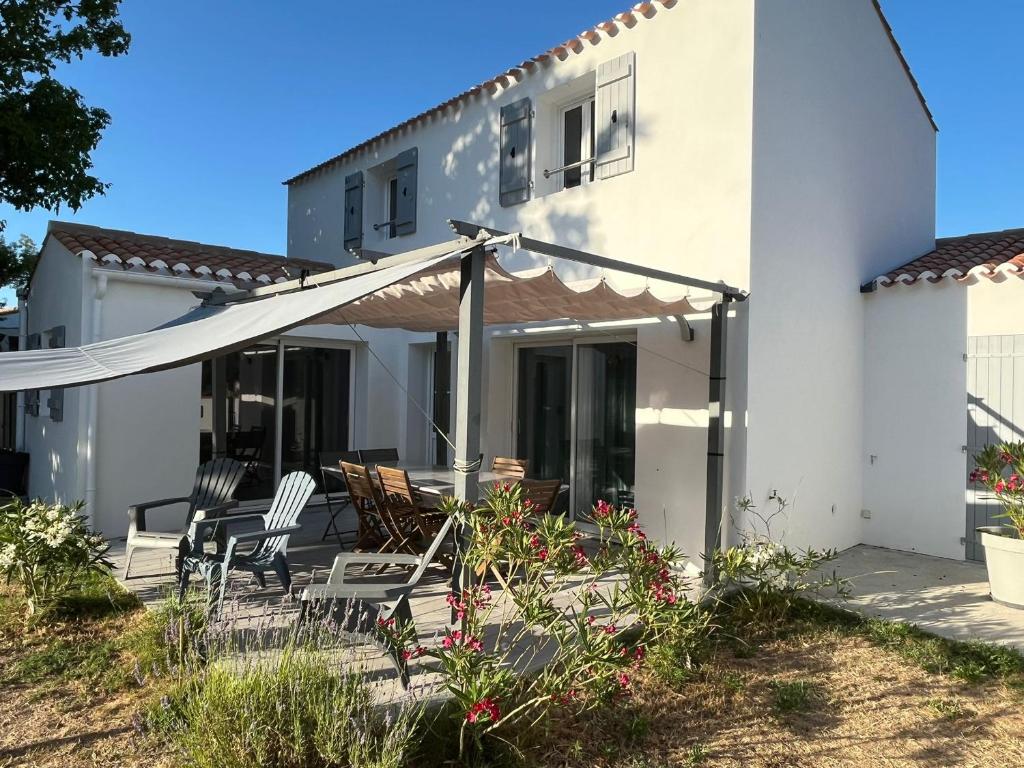 une maison blanche avec des chaises et un parasol dans l'établissement Belle maison à Barbâtre, 800m plage, pour 7 personnes avec jardin clos, terrasse et WiFi gratuit - FR-1-823-69, à Barbâtre